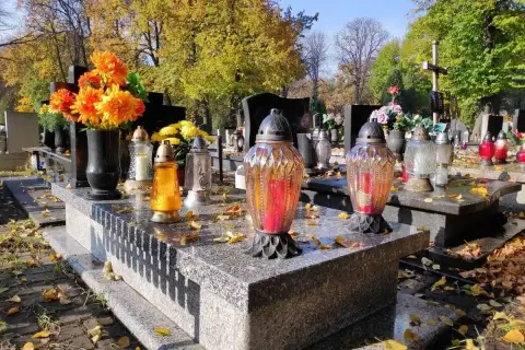 Jesienne miejsce na cmentarzu. Znicze i kwiaty na grobach, opadłe liście tworzą melancholijny nastrój.