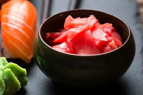 Miseczka z różowym, marynowanym imbirem obok sushi i wasabi. Idealny dodatek do japońskich przysmaków.