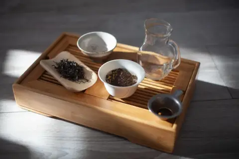 Zestaw do gongfu cha: drewniana taca, liście herbaty, czajniczek, miseczki i sitko.