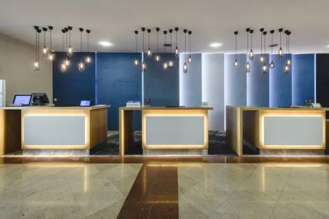 Recepcja hotelowa z trzema ladami, nowoczesnymi lampami i podświetlanymi panelami.