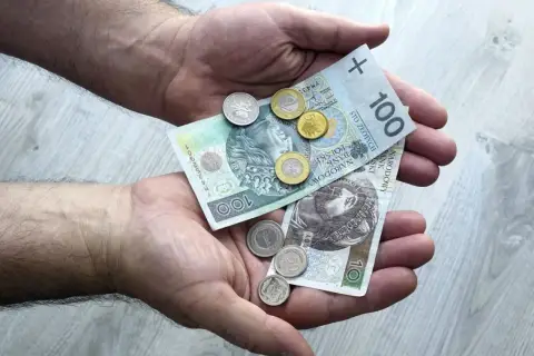 Dłonie trzymające polskie banknoty 100 zł i 10 zł oraz monety.
