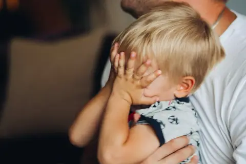 20 miesięczne dziecko budzi się w nocy, ukrywając twarz w dłoniach. Tata tuli go, próbując uspokoić.