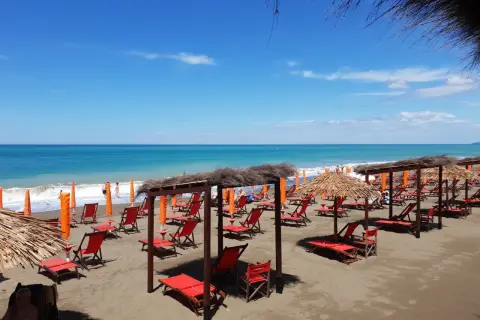 Plage de Marina di Bibbona avec des chaises longues rouges et des parasols de paille sous un ciel bleu éclatant.