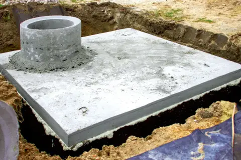 Betonowa płyta fundamentowa z kominem szamba, przygotowana do dalszych prac. Zastanawiasz się, ile kosztuje montaż szamba?