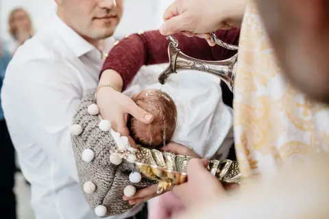 Woda święcona spływa na główkę niemowlęcia, rozpoczynając uroczysty obrzęd chrztu.
