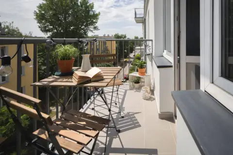 Przytulny balkon z drewnianym stolikiem i krzesłami, roślinami i lampkami. Zastanawiasz się, ile kosztuje balkon przyczepny?