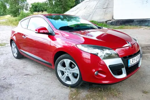 Czerwone Renault Megane Coupe 3 na tle betonowej konstrukcji i zieleni.