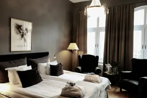 Ett elegant hotellrum inredning med dubbelsäng, bekväma fåtöljer, en kristallkrona och konst på väggen.