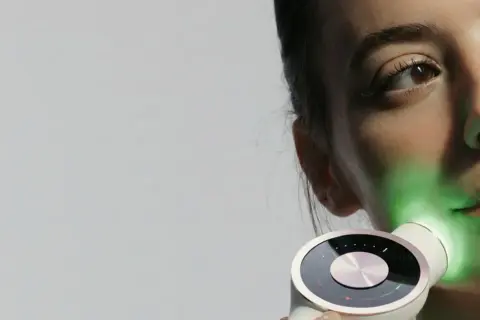 Une femme utilise un appareil de luminothérapie LED pour le visage, projetant une lumière verte apaisante.
