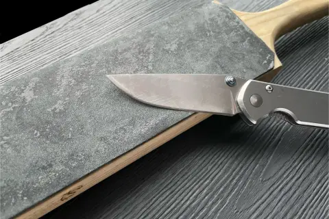 En kniv slipas mot en grov slipsten med trähandtag.