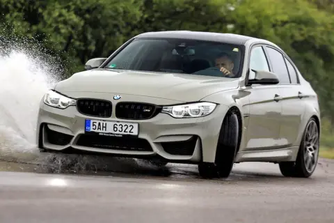 Szary BMW F80 M3 pokonuje kałużę, tworząc efektowny rozbryzg wody.