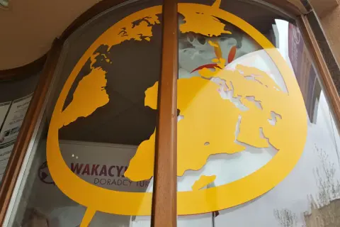 Żółta mapa świata na szybie biura podróży z widocznymi ofertami wakacyjnymi.