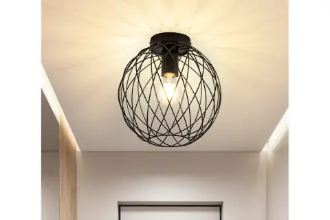 Nowoczesna lampa sufitowa z czarną, drucianą kulą i widoczną żarówką, tworząca ciekawe cienie na suficie.