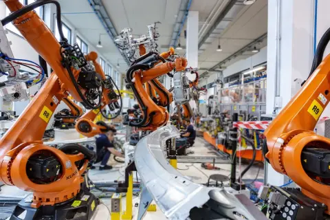 Pomarańczowe ramiona robotów KUKA pracują w fabryce, tworząc przyszłość. To zaawansowana robota automatyka.