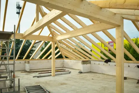 Struttura in legno per la realizzazione di tetti, con travi a vista e muri in blocchi di cemento. In sottofondo, attrezzature da cantiere.
