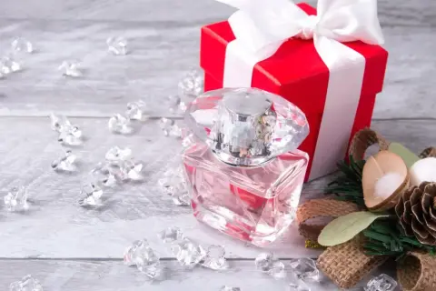Eleganckie perfumy w szklanej butelce, czerwone pudełko z kokardą i ozdoby. Idealny pomysł, jak zapakować perfumy na prezent.