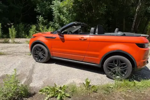 Orange Range Rover Evoque Cabrio, offen, steht auf einem Schotterweg. Mögliche Probleme mit dem Verdeck?
