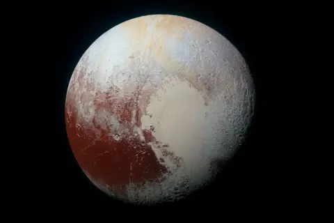 Pluton w całej okazałości, z czerwonymi i białymi plamami na powierzchni, unoszący się w czerni kosmosu.