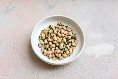 Eine Schüssel mit gekochten, hellen Bohnen, verfeinert mit gehackter Petersilie. Diese Fagioli Borlotti sind ein köstlicher deutscher Klassiker.
