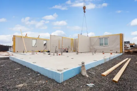 Budowa domu z prefabrykatu keramzytowego. Dźwig podnosi element ściany na fundament.