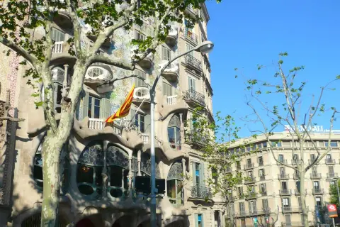 La Casa Batlló, joya modernista, luce su fachada ondulante y colorida bajo el sol. Una bandera catalana ondea, celebrando Sant Jordi.