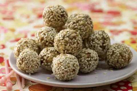 Ein Haufen köstlicher Energy Balls, umhüllt von Sesam, auf einem Teller. Perfekt für einen schnellen Energieschub!