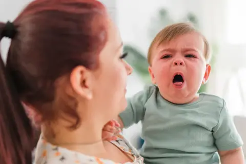 Mama z rudymi włosami tuli płaczące dziecko. Może to być objaw RSV u malucha, który potrzebuje troski.