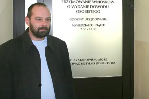 Mężczyzna czeka na informację, ile kosztuje wyrobienie dowodu osobistego. Tablica informuje o godzinach urzędowania.