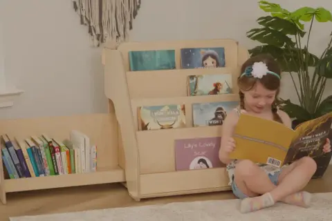 A young girl reads a book next to a DIY Montessori bookshelf filled with children's books.