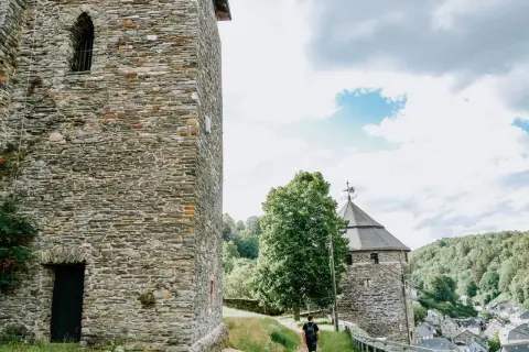 Ein Mann spaziert auf einem Weg zur Burg Monschau, vorbei an alten Steintürmen und grünen Hügeln.