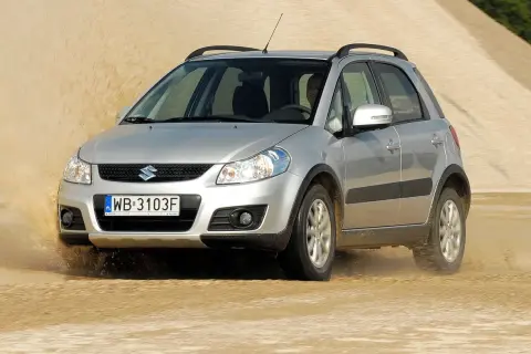Srebrny Suzuki SX4 pokonuje piaszczystą wydmę, wzbijając tumany kurzu.