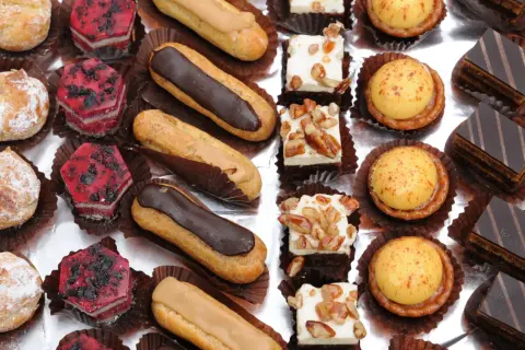 Variedad de petit fours: éclairs de chocolate y caramelo, pastelitos de frutas rojas, cuadrados de crema con nueces, tartas de crema amarilla y pastelitos de chocolate.