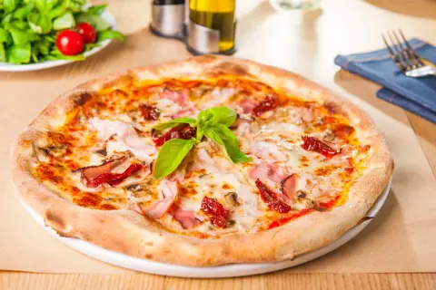Pizza garnie de jambon, champignons et tomates séchées, sur une pâte à pizza moelleuse. Une feuille de basilic frais couronne le tout.