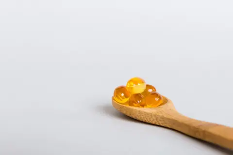 Houten lepel met gele capsules, mogelijk ter bestrijding van vitamine d tekort duizeligheid.