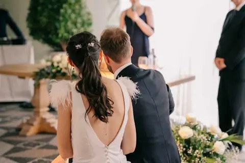 Novia con coleta baja adornada con horquillas, ideal para peinados para boda civil. El novio, de traje oscuro, la acompaña.