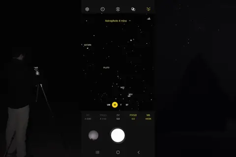 Mężczyzna robi zdjęcie nocnego nieba z Saturnem i Plutonem za pomocą telefonu Samsung. Tryb Astrophoto ustawiony na 4 minuty.