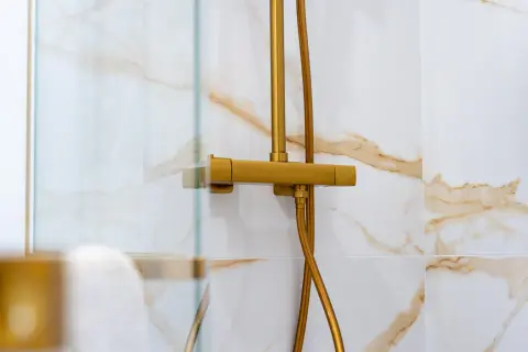 Robinet de douche doré, avec un pommeau réglable en hauteur, sur un mur carrelé de marbre blanc et or.