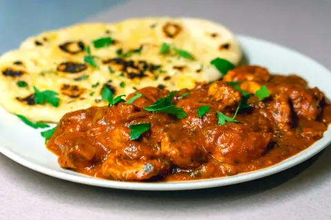 En krämig chicken tikka masala med bitar av kyckling i en smakrik tomatsås, serverad med fluffigt naanbröd.
