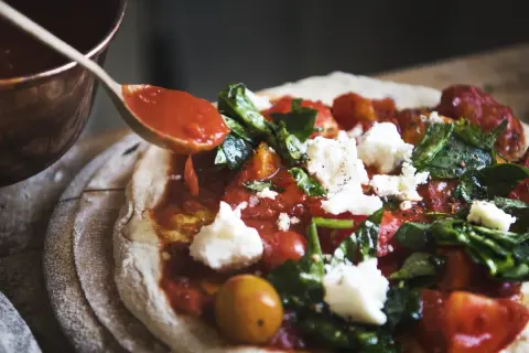 Sos pomidorowy dodawany łyżką do pizzy z serem i bazylią.