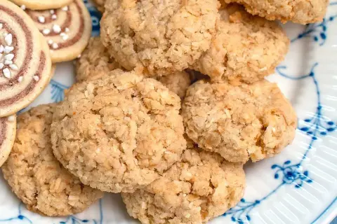 En hög med hembakade havrekakor, perfekta för ett enkelt havrekakor recept. Bredvid syns några rullade kakor med pärlsocker.