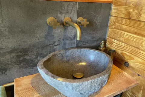 Lavabo in pietra grezza, rubinetteria in ottone e rivestimento in legno: perfette idee bagno montagna per un'atmosfera rustica e accogliente.