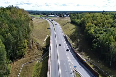 Droga krajowa 22 przecina gęsty las. Samochody poruszają się po wielopasmowej jezdni, otoczonej zielenią.