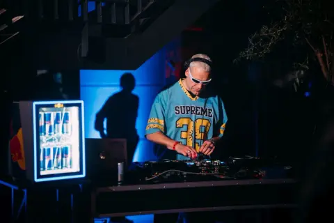 DJ Inox w niebieskiej koszulce z numerem 39 gra muzykę na konsoli DJ-skiej.