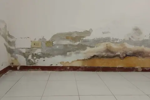 Muri con intonaco antiumido scrostato e macchie di umidità, prese elettriche visibili.