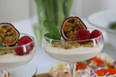 Två glas med len vit chokladmousse, toppade med passionsfrukt, hallon och mynta. En läcker dessert som passar perfekt till fikat.