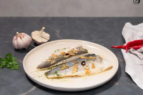 Dos filetes de lubina a la donostiarra, con láminas de ajo dorado, perejil picado y un toque de guindilla.