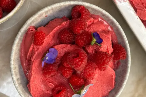 En skål med krämig hallonyoghurtglass toppad med färska hallon och små violer. En härlig sommardessert.