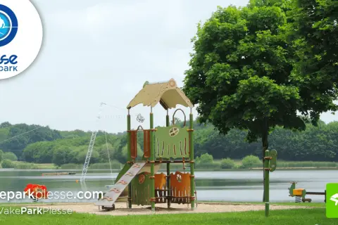 Aire de jeux près de l'étang de Buhel, avec un toboggan et un portique. Le logo WakePark Plessé est visible.