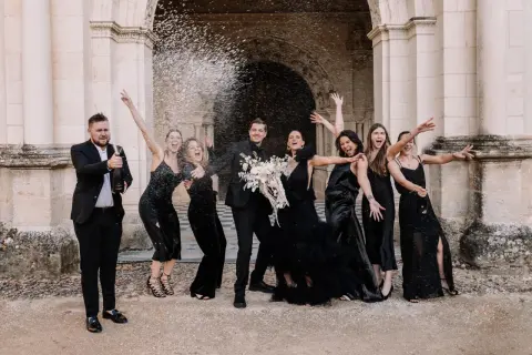 Un groupe joyeux célèbre un mariage noir et blanc, le marié ouvrant une bouteille de champagne sous une pluie de confettis.
