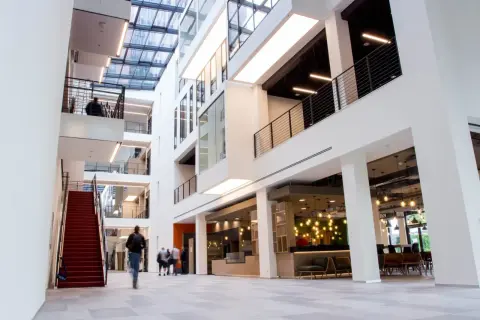 Helles, modernes Gebäude mit Glasdach und roten Treppen. Menschen gehen durch die Lobby des ISM Frankfurt.